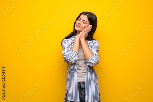 Teenager girl over yellow wall making sleep gesture in dorable expression © luismolinero