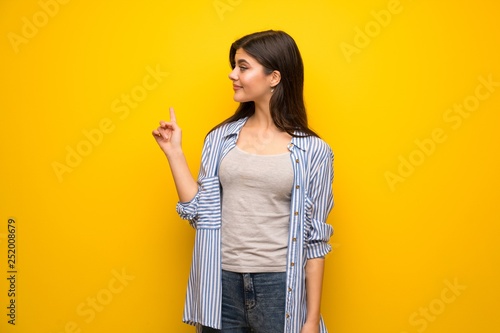 Teenager girl over yellow wall pointing back