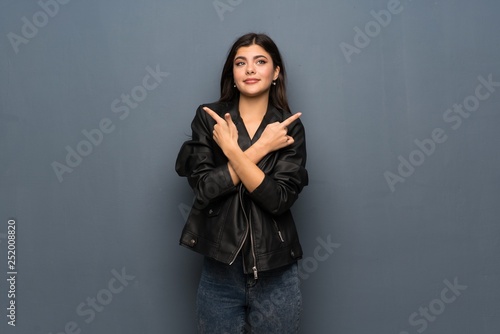 Teenager girl over grey wall pointing to the laterals having doubts