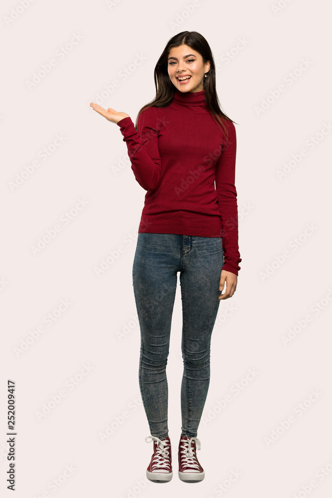 A full-length shot of a Teenager girl with turtleneck holding copyspace imaginary on the palm to insert an ad over isolated background A full-length shot of a Teenager girl with turtleneck holding copyspace imaginary on the palm to insert an ad over isolated background
