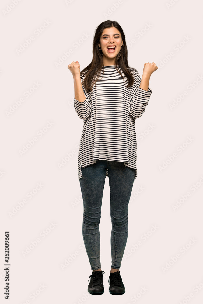 A full-length shot of a Teenager girl with striped shirt celebrating a victory in winner position over isolated background A full-length shot of a Teenager girl with striped shirt celebrating a victory in winner position over isolated background