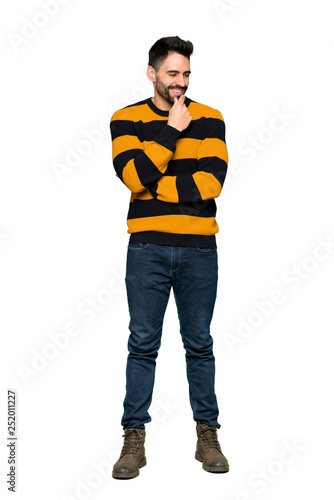 Full-length shot of Handsome man with striped sweater looking to the side with the hand on the chin on isolated white background
