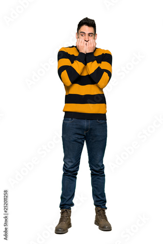 Full-length shot of Handsome man with striped sweater is a little bit nervous and scared putting hands to mouth on isolated white background