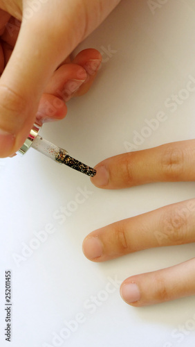 Hand applying glittering nail polish onto finger nail.