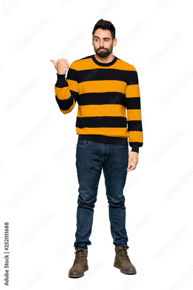 Full-length shot of Handsome man with striped sweater unhappy and pointing to the side on isolated white background Full-length shot of Handsome man with striped sweater unhappy and pointing to the side on isolated white background