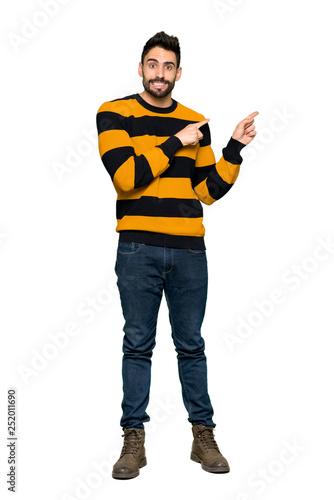 Full-length shot of Handsome man with striped sweater frightened and pointing to the side on isolated white background © luismolinero