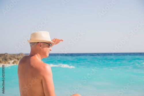 man on beach rear view guy wearing summer hat, standing back looking to sea blue sky horizon, vacation concept of freedom travel ocean