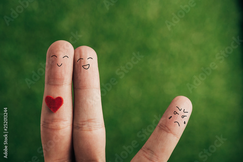 cropped view of fingers as happy couple and jealous person on green