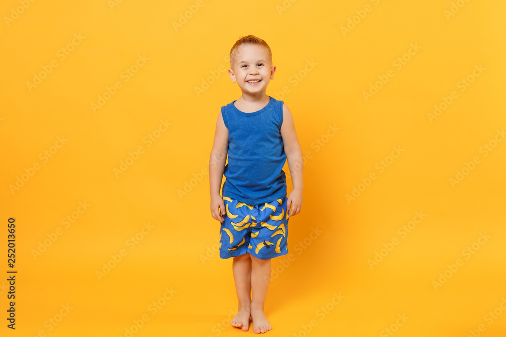 Smiling fun kid boy 3-4 years old wearing blue beach summer clothes isolated on bright yellow orange wall background, children studio portrait. People, childhood lifestyle concept. Mock up copy space. Smiling fun kid boy 3-4 years old wearing blue beach summer clothes isolated on bright yellow orange wall background, children studio portrait. People, childhood lifestyle concept. Mock up copy space.
