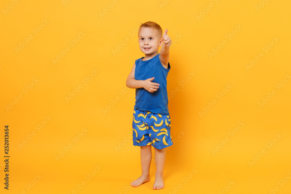 Smiling fun kid boy 3-4 years old wearing blue beach summer clothes isolated on bright yellow orange wall background, children studio portrait. People, childhood lifestyle concept. Mock up copy space. Smiling fun kid boy 3-4 years old wearing blue beach summer clothes isolated on bright yellow orange wall background, children studio portrait. People, childhood lifestyle concept. Mock up copy space.