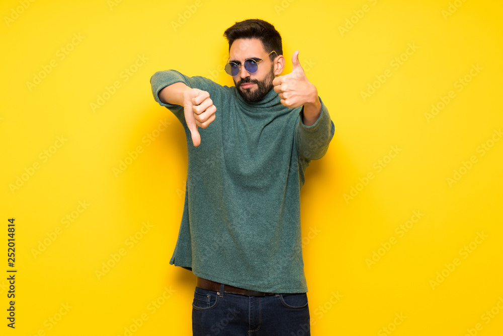 Handsome man with sunglasses making good-bad sign. Undecided between yes or not Handsome man with sunglasses making good-bad sign. Undecided between yes or not