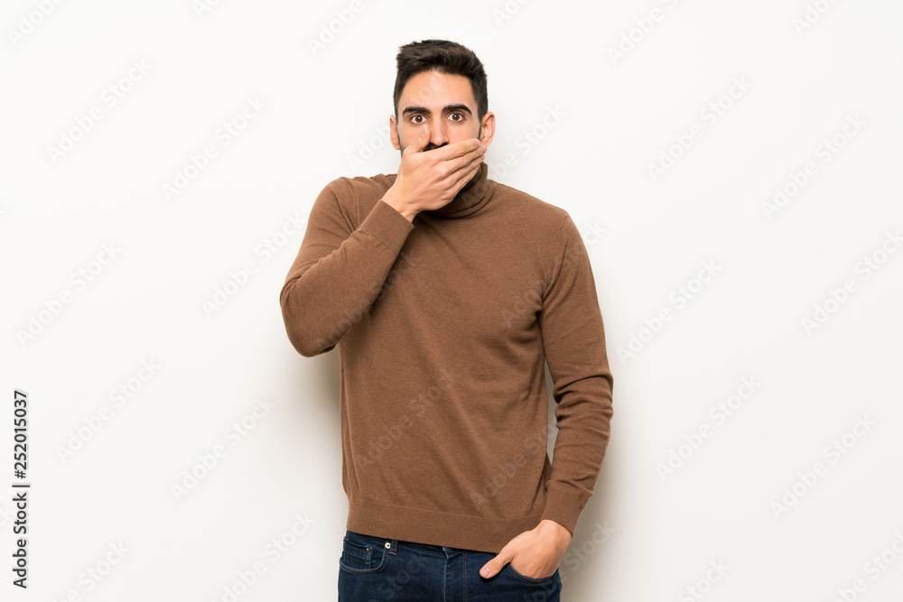 Handsome man over white wall covering mouth with hands for saying something inappropriate Handsome man over white wall covering mouth with hands for saying something inappropriate