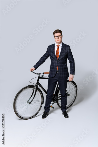 stylish businessman in suit standing with bicycle on grey