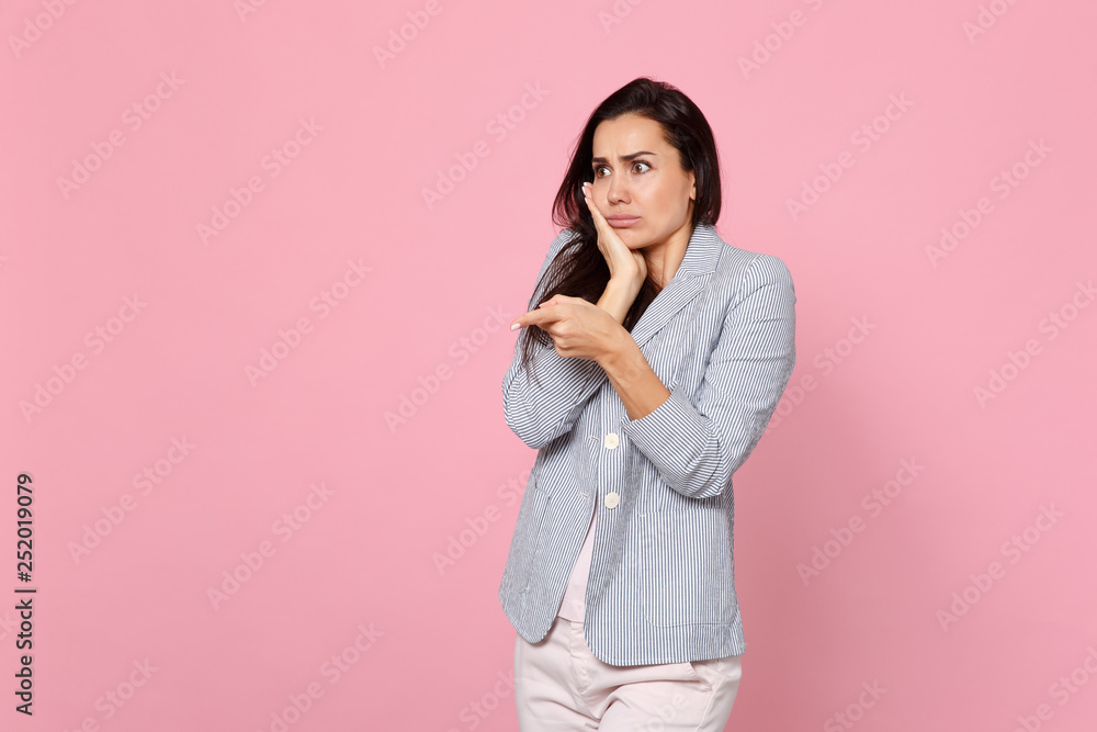 Shocked perplexed young woman in striped jacket putting hand on cheek, pointing index finger aside isolated on pink pastel background. People sincere emotions, lifestyle concept. Mock up copy space. Shocked perplexed young woman in striped jacket putting hand on cheek, pointing index finger aside isolated on pink pastel background. People sincere emotions, lifestyle concept. Mock up copy space.