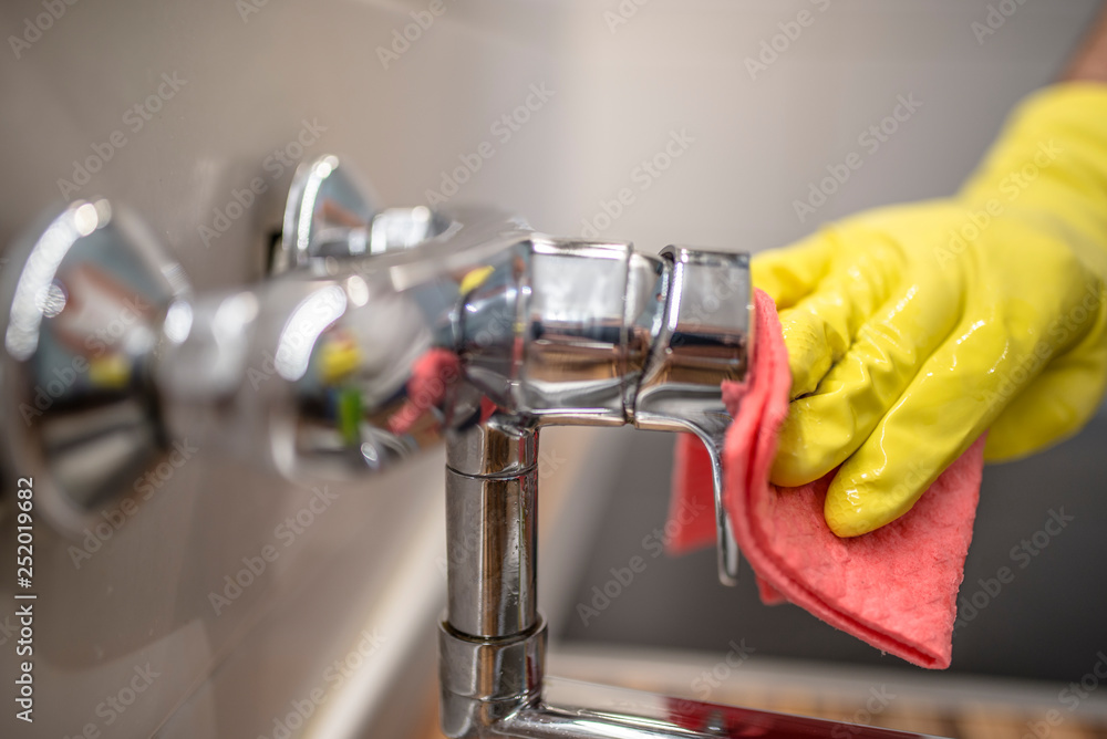 Young handsome man wiping faucet in kitchen. House cleaning service or husband doing chores Young handsome man wiping faucet in kitchen. House cleaning service or husband doing chores