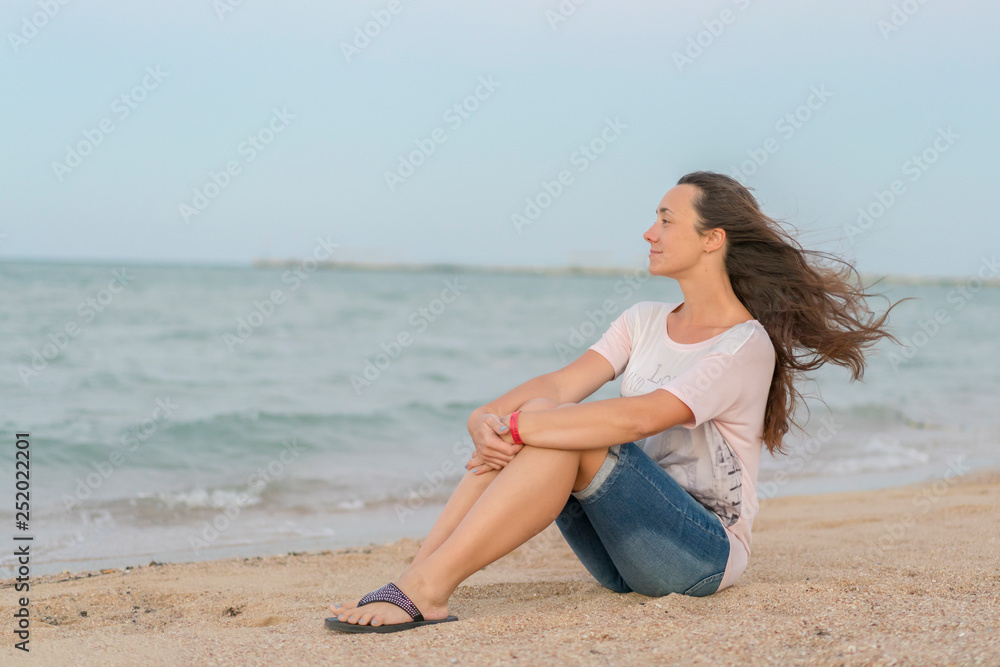 Beautiful girl sitting on the beach. Middle aged woman resting at beach near the sea. young, beautiful woman with long flowing hair on the beach Beautiful girl sitting on the beach. Middle aged woman resting at beach near the sea. young, beautiful woman with long flowing hair on the beach