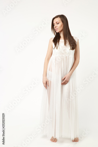 Full length photo fashion model woman wearing evening dress gown posing isolated on white wall background studio portrait. Beautiful brunette long hair girl. Mock up copy space. Peignoir for pregnant.