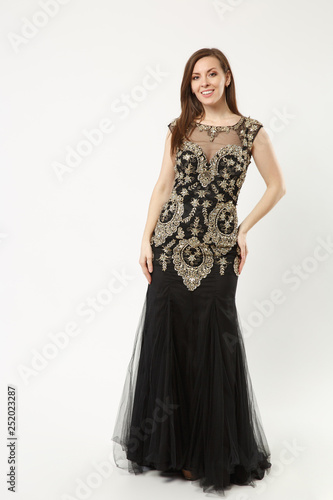 Full length photo of fashion model woman wearing elegant evening dress gown posing isolated on white wall background studio portrait. Brunette long hair girl. Mock up copy space. Black dress face view