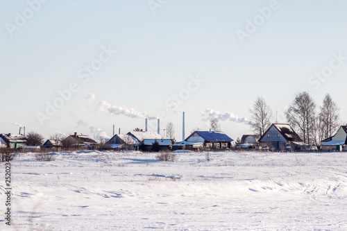 Bright winter landscape with blue sky in the spring sun and in the background village and industrial pipes with smoke in the environment. Сoncept of pollution and global warming. © Fotony76
