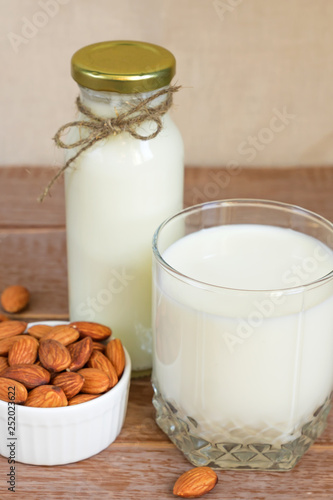Homemade Almond milk in a bottle and nuts in white porcelain bowl on wooden background