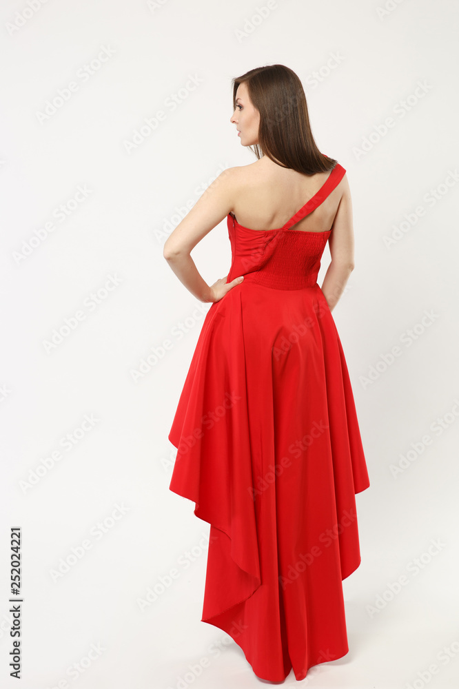 Full length photo of fashion model woman wearing elegant evening dress red gown posing isolated on white wall background studio portrait. Brunette long hair girl. Mock up copy space. Back rear view. Full length photo of fashion model woman wearing elegant evening dress red gown posing isolated on white wall background studio portrait. Brunette long hair girl. Mock up copy space. Back rear view.