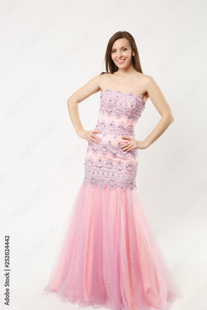 Full length photo of fashion model woman wearing elegant evening dress gown posing isolated on white wall background studio portrait. Brunette long hair girl. Mock up copy space. Pink dress face view.