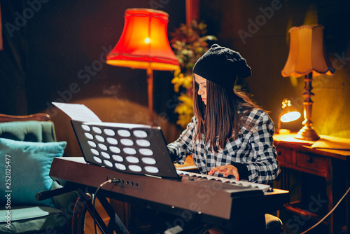 Beautiful young Caucasian woman with hat on head sitting and playing clavier in home studio. photo