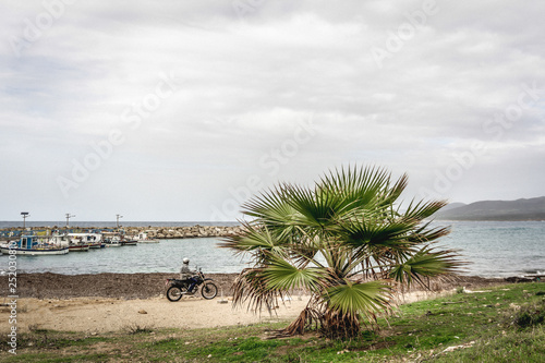 Peyia, Paphos District/Cyprus - February 2019: A man is driving a motorcycle near the Agios Georgios Peyeia Akamas beach.  photo