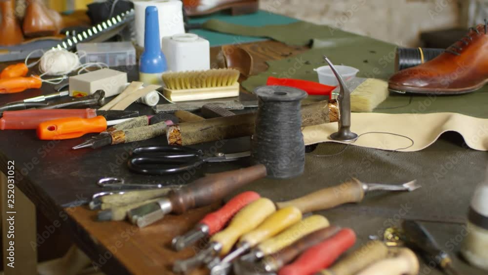 Tilt up shot of shoemaker tools, instruments, materials and supplies on work desk in the workshop Tilt up shot of shoemaker tools, instruments, materials and supplies on work desk in the workshop