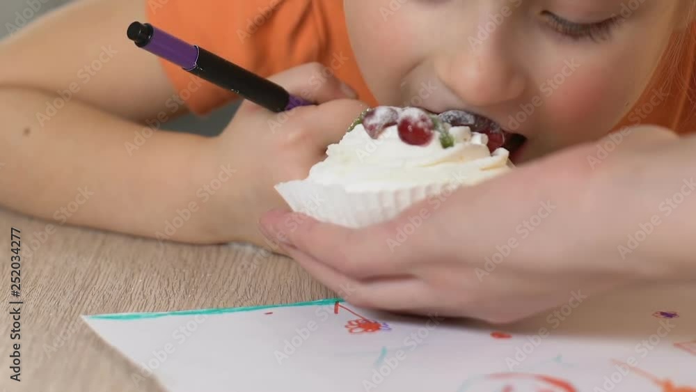 Mom giving little girl tasty cream cake, daughter biting it snack while painting Mom giving little girl tasty cream cake, daughter biting it snack while painting