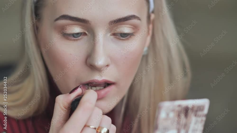 Blond girl paints her lips with lipstick with a dull red color. Blond girl paints her lips with lipstick with a dull red color.