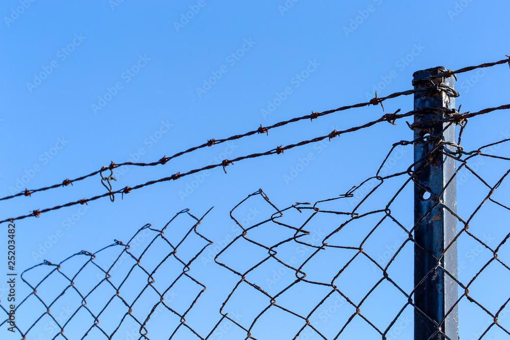 Barbed wire over old wire fnce with blue sky Barbed wire over old wire fnce with blue sky