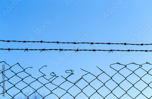 Barbed wire over old wire fence with blue sky