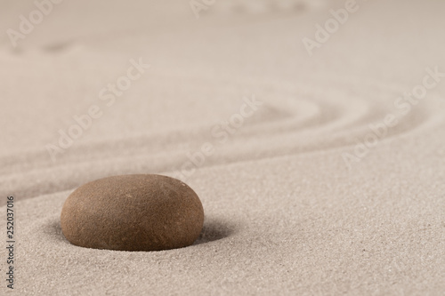 Concentration trough focus on a zen meditation stone. Round rock in sand texture background. Concept for yoga or spa welness treatment.