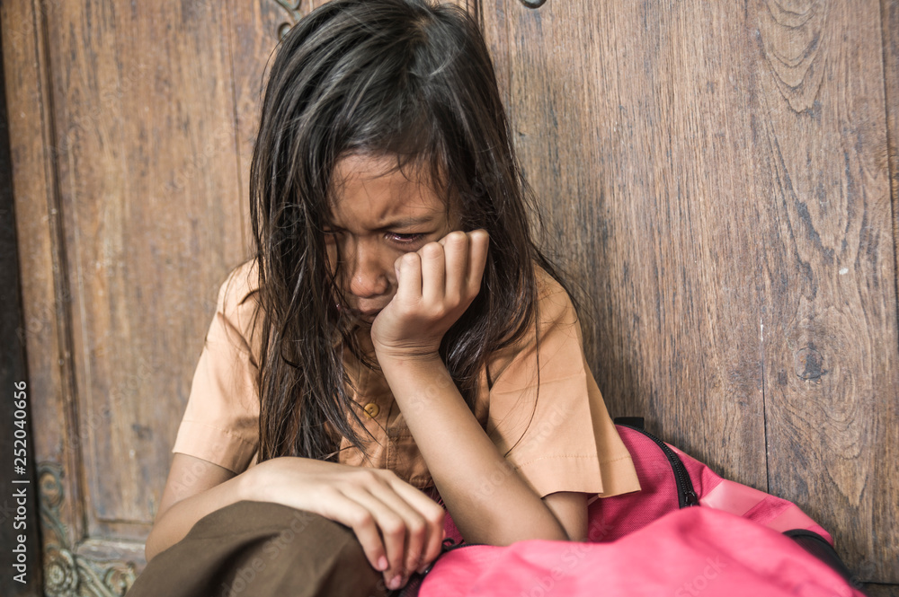 7 or 8 years child in school uniform sitting outdoors on the floor crying sad and depressed holding her backpack suffering bullying and abuse problem feeling helpless 7 or 8 years child in school uniform sitting outdoors on the floor crying sad and depressed holding her backpack suffering bullying and abuse problem feeling helpless