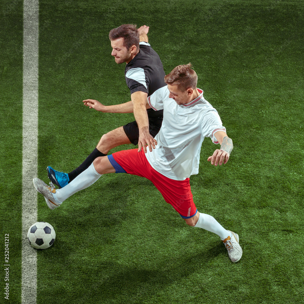 Football player tackling for ball over green grass background. Professional male soccer players in motion at stadium. Fit jumping men in action, jump, movement at game.