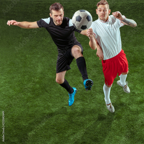 Football player tackling for ball over green grass background. Professional male soccer players in motion at stadium. Fit jumping men in action  jump  movement at game.