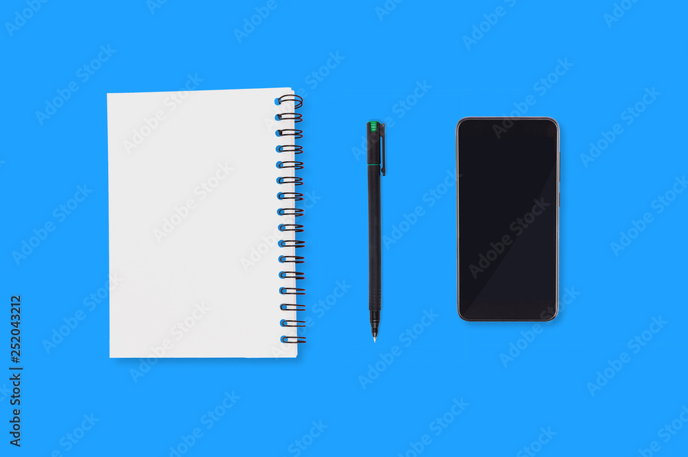 Office supplies paper notepad with blank sheet plastic pen and black smartphone spread out on blue table. Top view. Business concept. Copy space for your text Office supplies paper notepad with blank sheet plastic pen and black smartphone spread out on blue table. Top view. Business concept. Copy space for your text