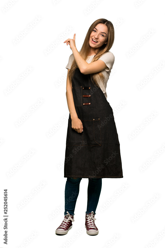 Full body Young woman with apron pointing back with the index finger on isolated background Full body Young woman with apron pointing back with the index finger on isolated background