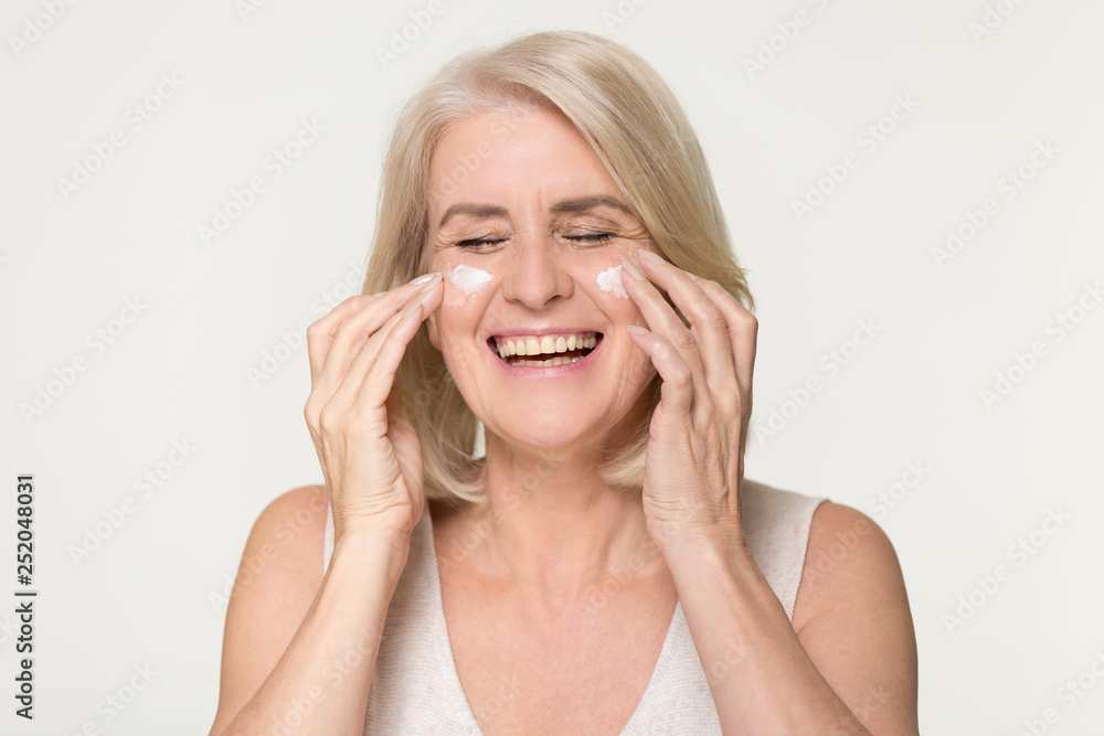 Happy old woman apply anti aging cream isolated on background Happy old woman apply anti aging cream isolated on background