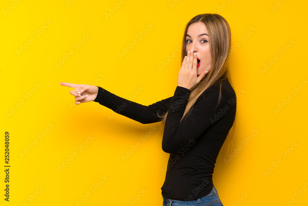 Young pretty woman over yellow background pointing finger to the side with a surprised face Young pretty woman over yellow background pointing finger to the side with a surprised face
