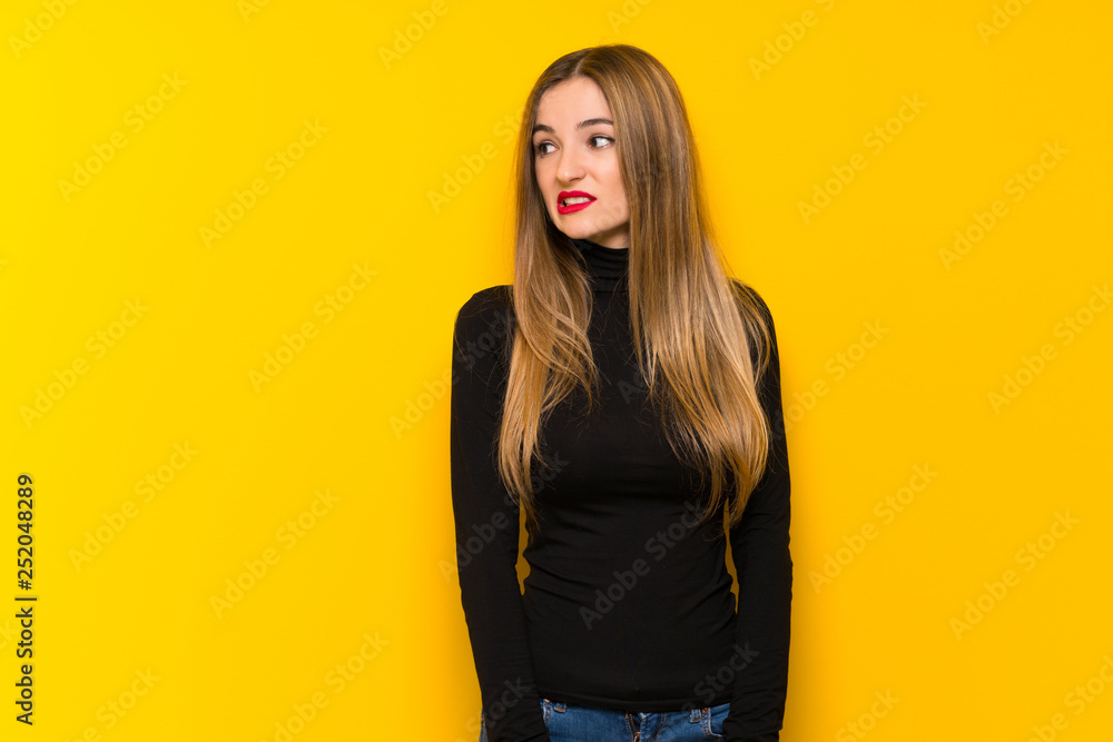 Young pretty woman over yellow background is a little bit nervous and scared pressing the teeth