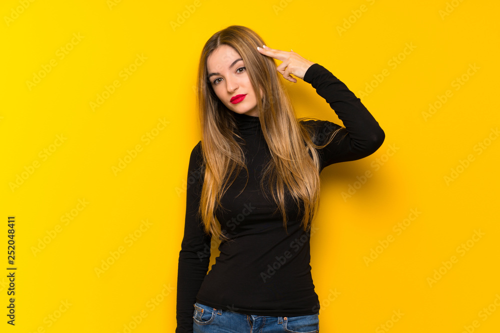 Young pretty woman over yellow background with problems making suicide gesture Young pretty woman over yellow background with problems making suicide gesture
