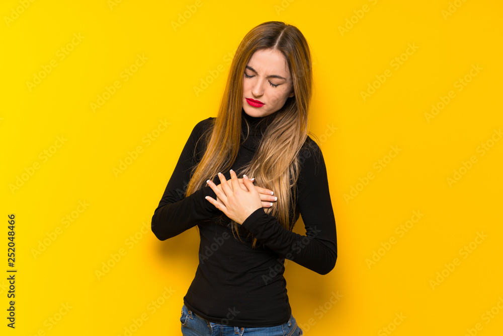 Young pretty woman over yellow background having a pain in the heart Young pretty woman over yellow background having a pain in the heart