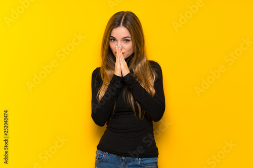 Young pretty woman over yellow background keeps palm together. Person asks for something