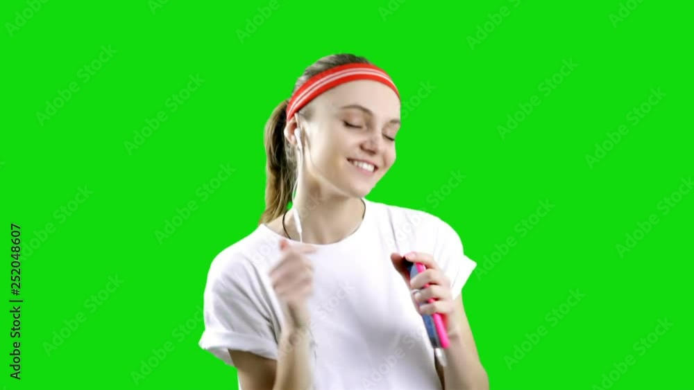 Happy young woman in sports clothing smiling and holding smart phone and listen music on green background. Chroma key Happy young woman in sports clothing smiling and holding smart phone and listen music on green background. Chroma key