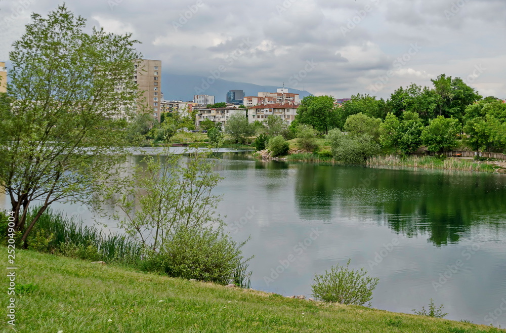 Spring panorama of a part of residential district neighborhood along a lake with green trees, shrubs and flowers, Drujba, Sofia, Bulgaria 