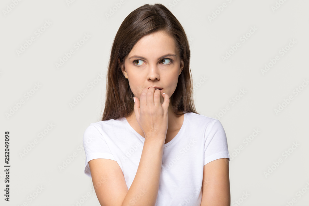 Nervous insecure young woman biting nails isolated on grey background Nervous insecure young woman biting nails isolated on grey background