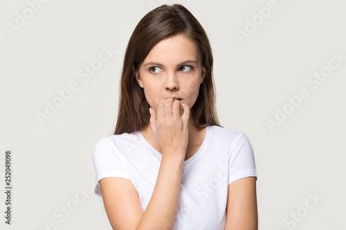 Nervous insecure young woman biting nails isolated on grey background