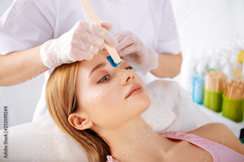 Specialist putting depilatory cream on line between eyebrows